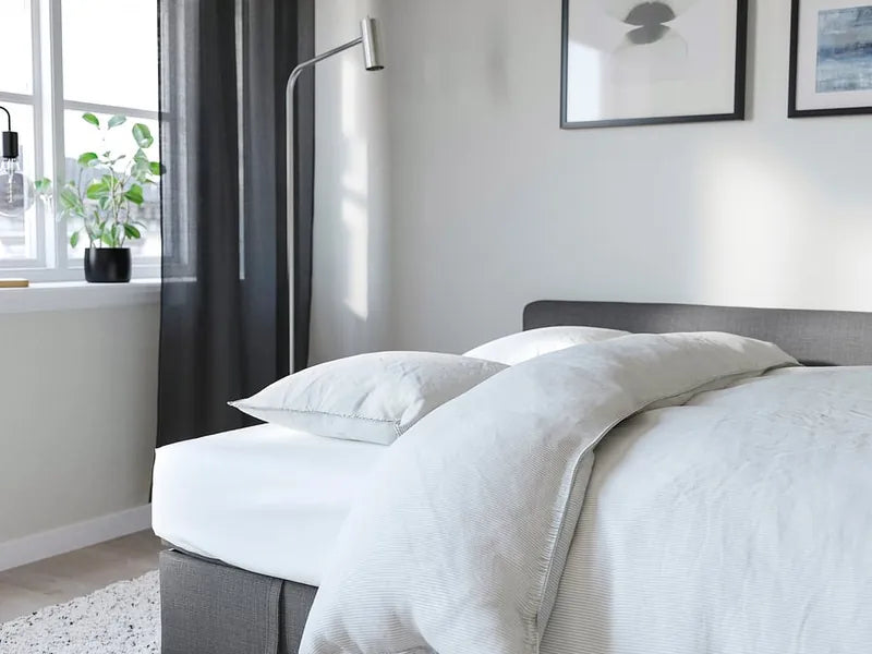 The grey corner sofa bed opened out and made up with white bedding in a bright room