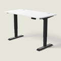 Electric standing desk, 140 × 70 cm, black frame and white top, with the memory handset under the front edge, on a pale grey background