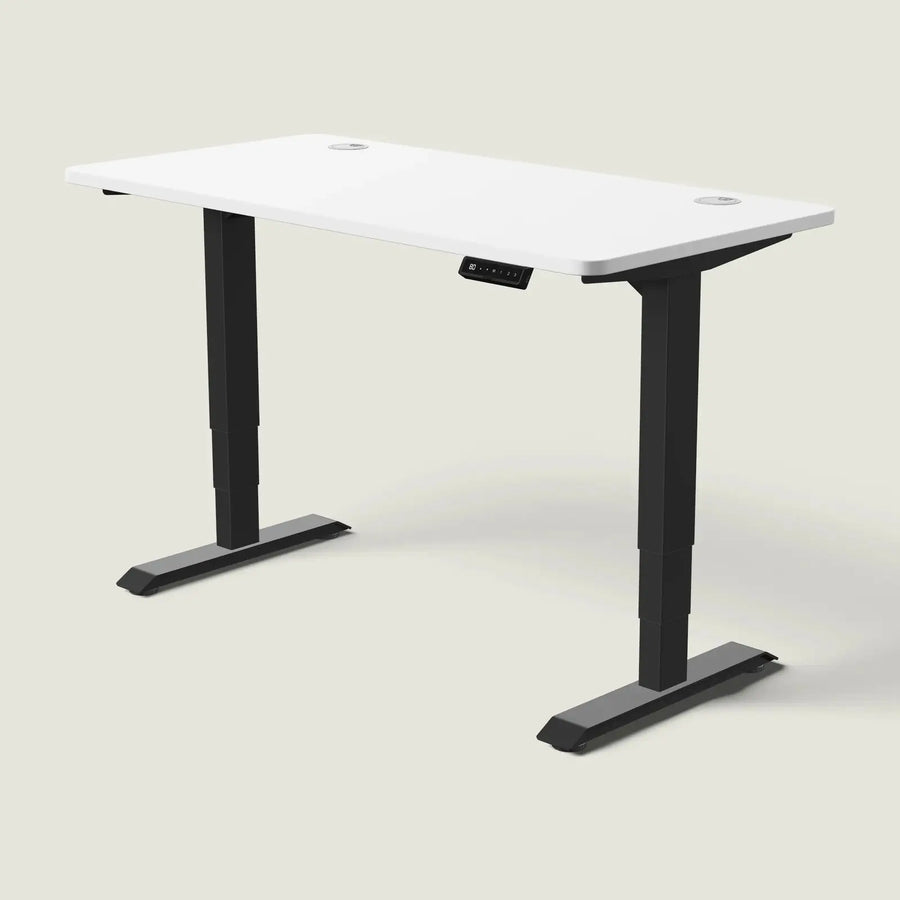 Electric standing desk, 140 × 70 cm, black frame and white top, with the memory handset under the front edge, on a pale grey background