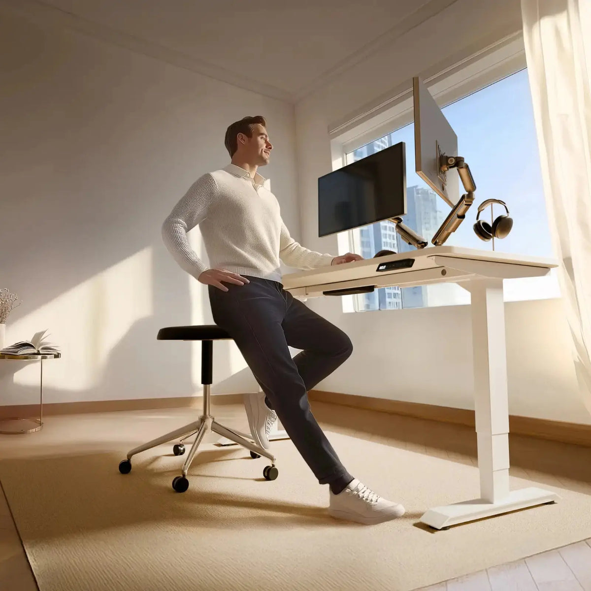 The desk with a white frame and a white top by a sunny window, a man perched on a stool beside it (monitor, arms and accessories not included)