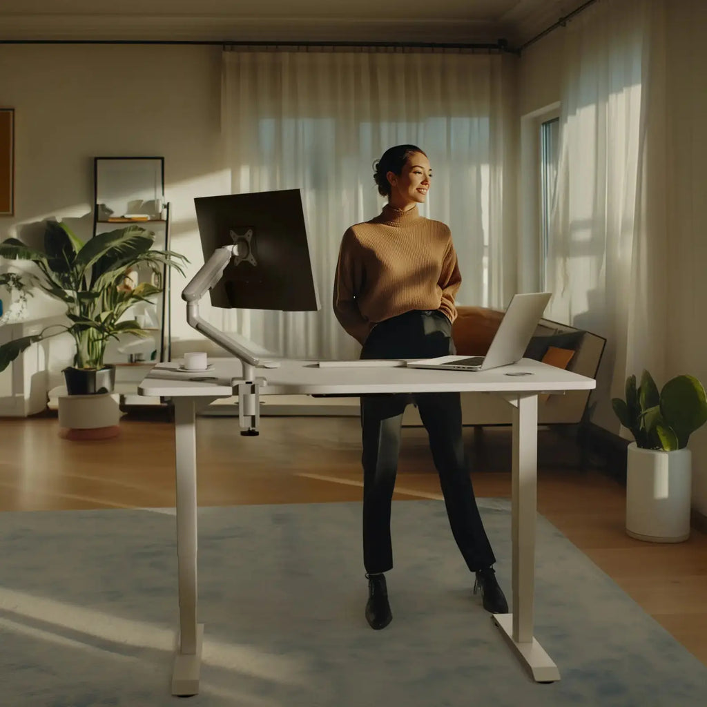 The desk with a white frame and a white top at standing height, a monitor arm clamped to the back edge (monitor, arm and laptop not included)